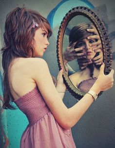 a woman in a pink dress holding a mirror with her face painted on the wall