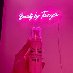 a person holding a pink spray bottle in front of a neon sign that says beauty by tonya