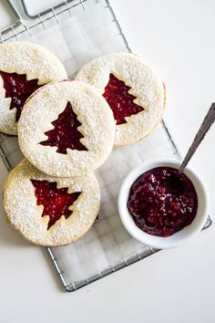 four cookies with jelly filling on a cooling rack next to a small bowl of jam