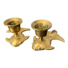 two brass candlesticks with fish heads on each one and a bowl in the middle