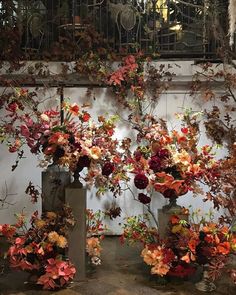 three vases filled with flowers sitting on top of a cement floor next to a wall