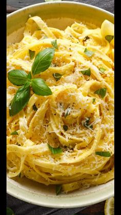 a bowl filled with pasta and garnished with fresh basil on the side next to sliced lemons