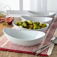 three white bowls filled with brussel sprouts on top of a wooden table