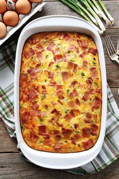 a casserole dish with bacon and eggs in it on a plaid cloth next to utensils