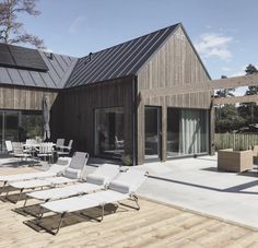 a wooden deck with lounge chairs and tables on top of it next to a house