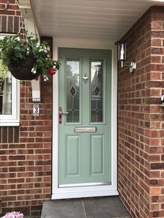 a green front door on a brick house with potted plants hanging from the side