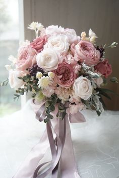 a bridal bouquet with pink and white flowers on a table in front of a window