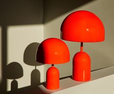 two orange lamps sitting next to each other on a white surface with shadows from the wall behind them