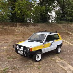 a small white and yellow car parked on top of a dirt field next to trees