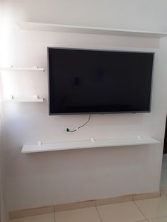 a flat screen tv mounted on the wall above a shelf in a room with tile flooring