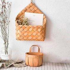 a wooden basket hanging on the wall next to a vase with flowers and a note