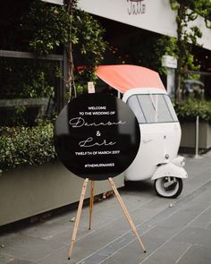 a black and white sign sitting on the side of a road next to a scooter