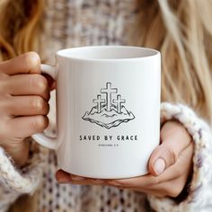 a woman holding a white coffee mug with the words saved by grace printed on it