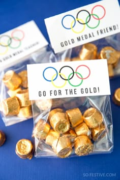 some gold coins are sitting in plastic bags on a blue surface with the olympic logo