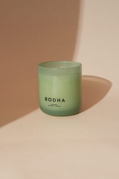 a candle sitting on top of a table next to a white wall with the word bodha printed on it