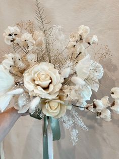 a bridal bouquet with white flowers and greenery is being held by someone's hand