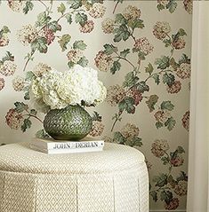 a vase with white flowers on top of a table next to a wallpapered room