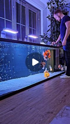 a man standing in front of an aquarium looking at flowers on the floor next to it