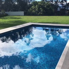 an empty swimming pool with blue tiles and grass in the back ground, reflecting clouds on the water