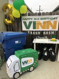 a table with a sign, trash can and balloons in the shape of a truck