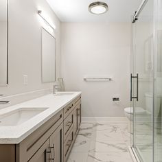 a white bathroom with marble counter tops and large mirrors on the wall, along with a walk in shower