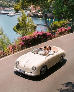 a man kissing a woman in a convertible car on the road near water and boats