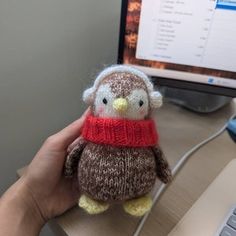 a hand holding a small knitted owl in front of a computer