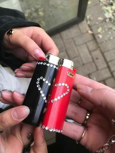 two people holding different types of lighters in their hands, one is red and the other is black