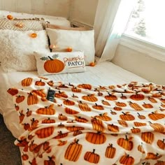 a bed with pumpkins on it and white pillows in front of a window,