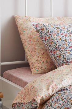 a bed with floral sheets and pillows on top of it in a white frame headboard