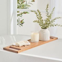 a white bath tub sitting next to a vase filled with flowers and two candles on top of it