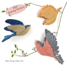 three felt birds sitting on top of a tree branch with leaves and branches around them