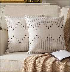 two pillows sitting on top of a couch next to a white chair with a book