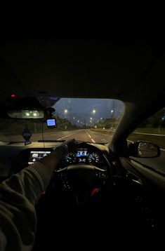 a person driving in the dark with their hands on the steering wheel and lights on