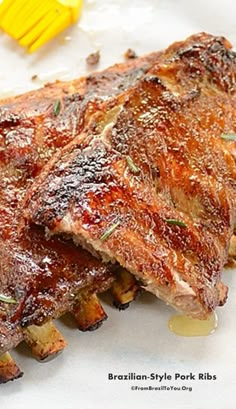 two pieces of meat sitting on top of a white plate next to yellow utensils