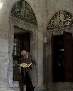 a man standing in front of a doorway reading a book with arabic writing on it