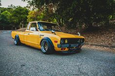 a yellow truck parked on the side of a road next to some trees and bushes