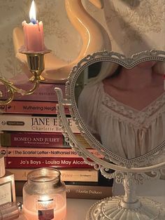 there is a candle and some books on the table with it's reflection in the mirror