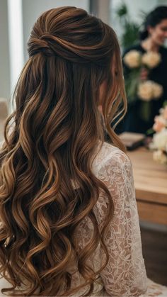 a woman with long, wavy hair sitting in front of a flowered table wearing a white dress