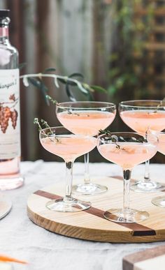 three glasses filled with pink wine sitting on top of a wooden tray