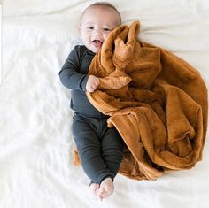 a baby laying on top of a bed covered in a brown blanket and smiling at the camera