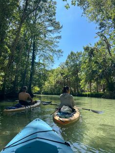 two people in kayaks paddling down a river surrounded by trees on a sunny day