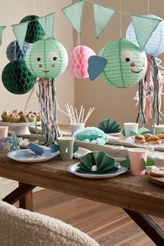 a wooden table topped with plates and cups filled with food next to hanging paper decorations