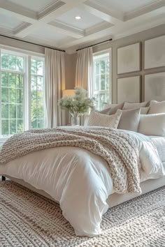 a large white bed sitting in a bedroom next to two windows and a rug on the floor