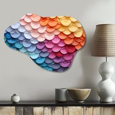 a large multicolored wall hanging on the side of a white wall next to a lamp