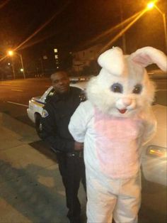 a man standing next to a police officer in bunny suit on the street at night