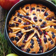 an apple and blueberry cobbler in a pie pan with fresh fruit on the side