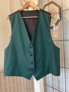 This tailored vest is made from a polyester blend in a beautiful shade of dark emerald green with a pattern (see the close-up for the pattern, not the colour!). It has the original buttons in the front, and the back and lining are made from black silky fabric. The measurements, taken with the vest lying flat, are: shoulder to shoulder, 16 inches; armpit to armpit, 25 inches; length, 26 inches in front and 24 inches in back; bottom edge, 25 inches. In very good condition. Winter Workwear Green Vest, Green Winter Workwear Vest, Elegant Green Vest For Formal Occasions, Elegant Green Formal Vest, Classic Green Formal Vest, Green Fitted Formal Vest, Formal Fitted Green Vest, Fitted Green Formal Vest, Elegant Fitted Green Vest