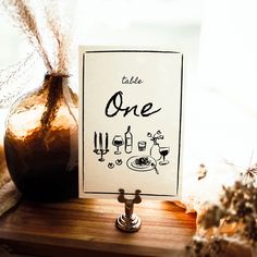 there is a sign that says table one next to a vase with flowers in it