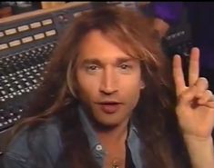 a man with long hair making the peace sign in front of a recording studio desk